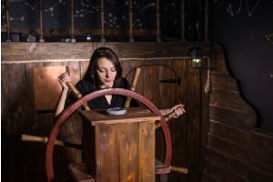 Young girl at the helm of a ship looking at compass in an escape room for a birthday party